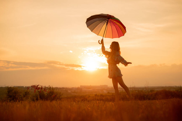 Young woman with umbrella dancing during sunset - Foto, afbeelding