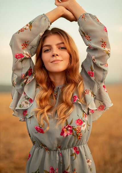 Young woman in floral dress standing in field - Photo, image