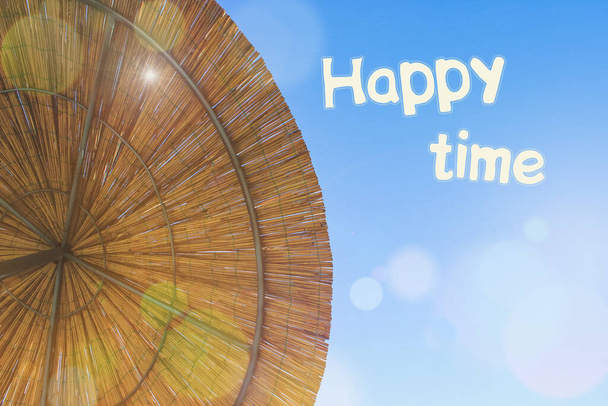 Die Sonne scheint durch den Schirm aus Bambus. Reetdachhintergrund mit der Inschrift glückliche Zeit. Kopierraum. Straw Beach Sonnenschirm Blick von oben. - Foto, Bild