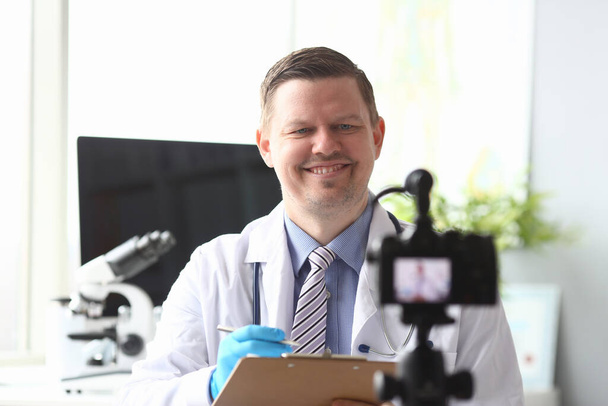 Doctor makes notes in folder in front video camera - Photo, Image