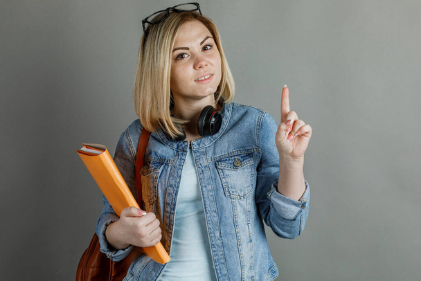 Un hermoso estudiante, con una mochila y un libro, muestra una mano de 1 a 5 sobre un fondo gris. La educación secundaria es el concepto de un Colegio Universitario
 - Foto, imagen