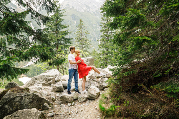 a young couple, a girl in a red dress, and a man in a white T-shirt and blue pants, are walking in the Tatra National Park in Polsha - Fotografie, Obrázek