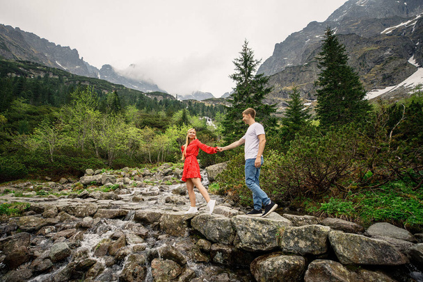 a young couple, a girl in a red dress, and a man in a white T-shirt and blue pants, are walking in the Tatra National Park in Polsha - Photo, image