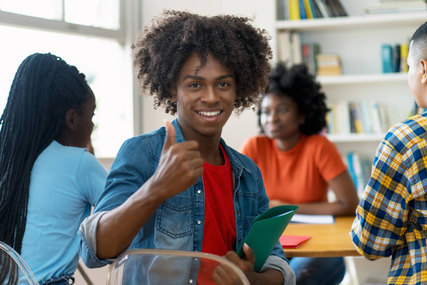 Succesvolle Afrikaans-Amerikaanse mannelijke student aan het bureau met een groep studenten in de klas - Foto, afbeelding