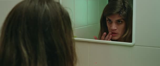 Eine junge Frau, die in den Spiegel schaut, bemerkt, dass sie aus ihrem Kopf blutet und Angst hat. Horrormord-Monster-Konzept. Nahaufnahme, filmisch. BMPCC 4K - Filmmaterial, Video
