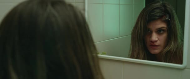 Young woman looking in the mirror discovering she is bleeding from her head, feeling scared. Horror murder monster concept. Close up, cinematic. BMPCC 4K - Footage, Video