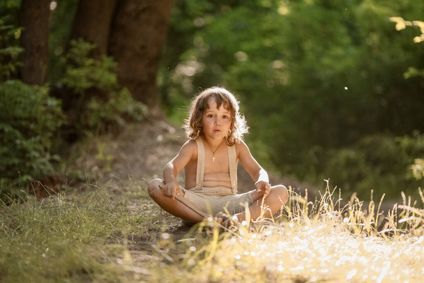 Ένα παιδί κάθεται ξυπόλητο στο έδαφος, πλυμένο με σταγόνες δροσιάς. - Φωτογραφία, εικόνα