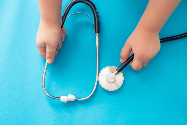 Children's hands hold a medical stethoscope on a blue background. - Foto, imagen