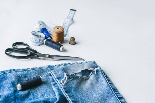 Ремесло, ремонт одежды. Рваные синие джинсы, швейные аксессуары на белом фоне. Концепция экономических вещей
. - Фото, изображение