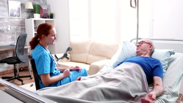 Female doctor talking old man lying in bed in a nursing home - Video, Çekim