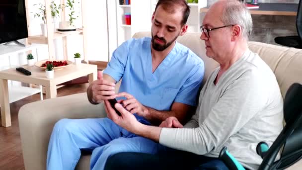 Young male doctor teaching old man to use his smartphone - Video, Çekim