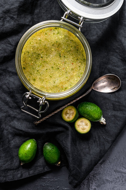 Ground green feijoa with sugar on a wooden cutting Board in a glass jar. Black background. Top view. - 写真・画像