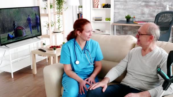 Caregiver nurse holding an old man hand while they are sitting on the couch - Video