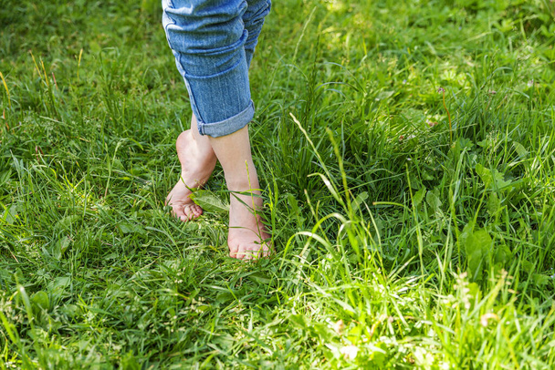 Two beautiful female feet walking on grass in sunny summer morning. Light step barefoot girl legs on soft spring lawn in garden or park. Healthy freedom relax concept - Photo, Image
