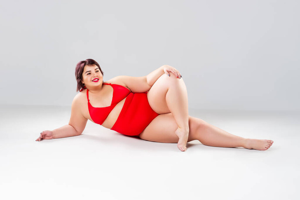 Plus size model in red swimsuit, fat woman in lingerie on gray background, overweight female body - 写真・画像