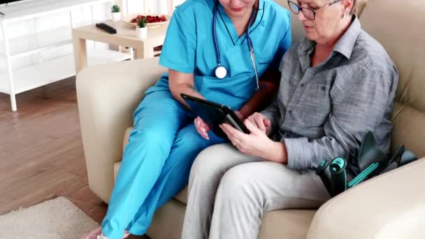 Yaşlı, emekli bir kadının tablet bilgisayarını kullanmasına yardım eden bir kadın. - Video, Çekim