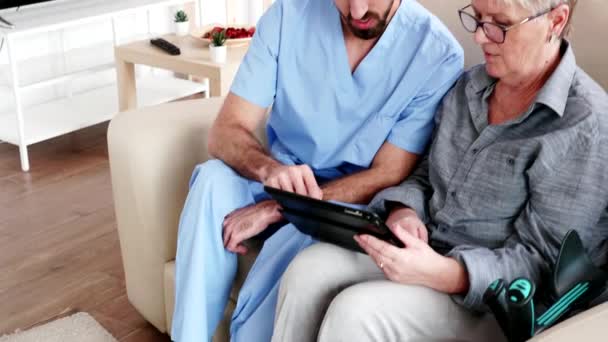 Male nurse teaching elderly old woman how to use her tablet PC - Filmati, video