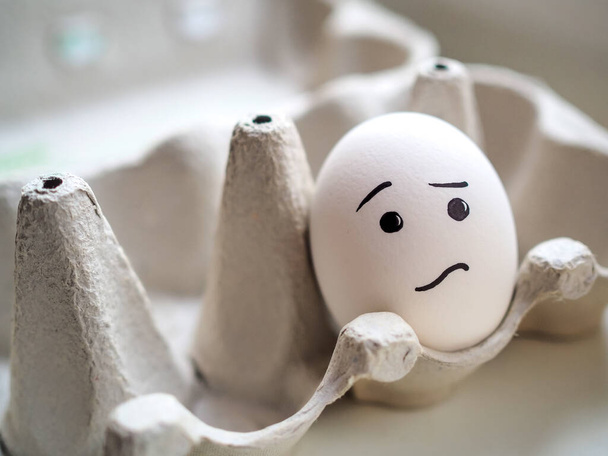 Lonely white egg with sad emoji lies in egg box - Foto, Bild