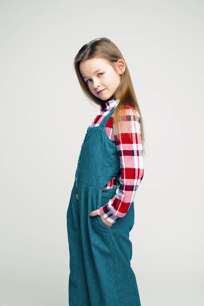 Fashionable portrait of a little girl in a denim overalls and a plaid shirt. children's studio shooting - Fotoğraf, Görsel