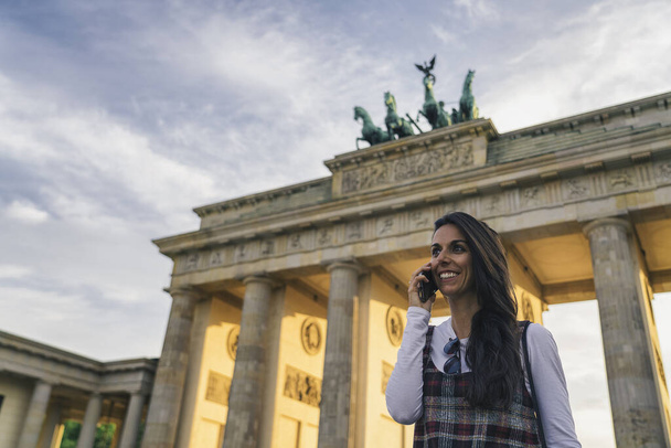 Cooles Lächeln und junge Frau im Handy-Gespräch am Brandenburger Tor in Berlin, Deutschland. - Foto, Bild