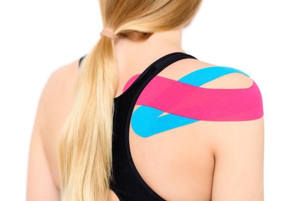 Studio shot of a female patient with kinesio tape on her shoulder and back, isolated over white. Kinesiology, physical therapy, rehabilitation background. - Photo, image
