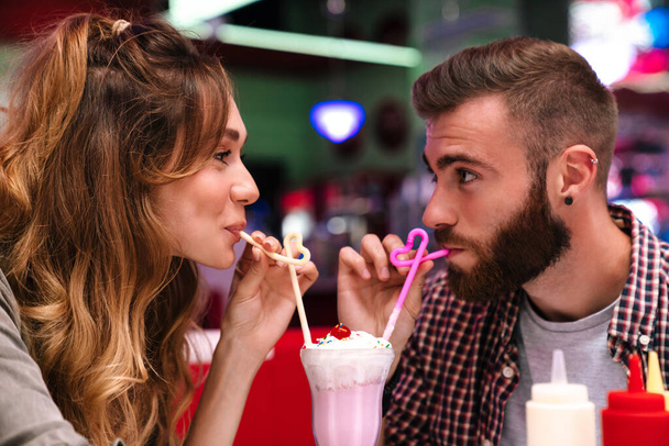 Photo of a cute positive young loving couple sit in retro bright cafe drinking cockail indoors. - Foto, imagen