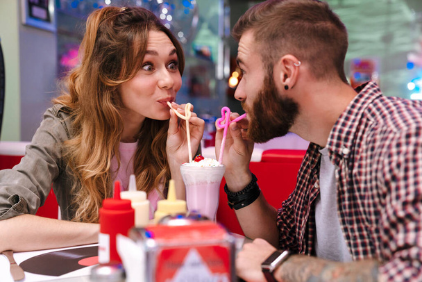 Photo of a cute positive young loving couple sit in retro bright cafe drinking cockail indoors. - Foto, Imagen