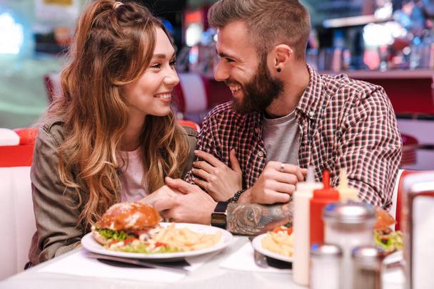 Photo of a cute pleased young loving couple in retro bright street food cafe hugging. - Foto, imagen