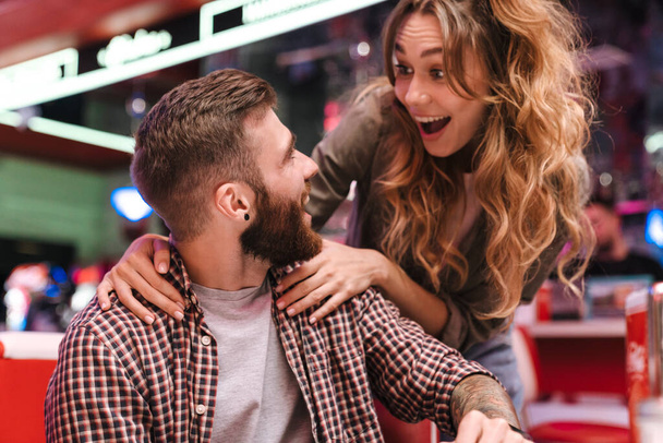 Photo of a cute surprised young loving couple in retro bright street food cafe. - Foto, imagen