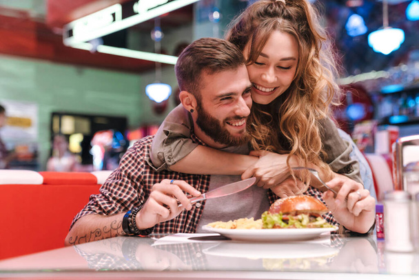 Photo of a cute happy positive young loving couple in retro bright street food cafe hugging. - Foto, imagen