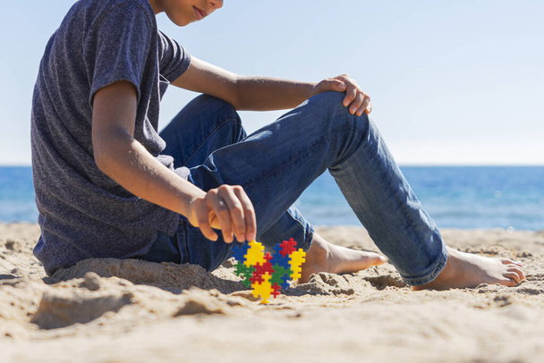 Konzept zum Tag des Autismus-Bewusstseins. Junge Teenager sitzt am Strand mit buntem Puzzle Autismus Bewusstsein Herz - Foto, Bild