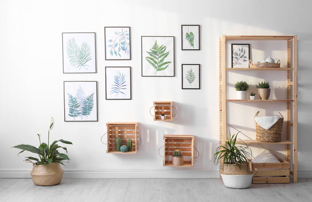Beautiful paintings of tropical leaves on white wall in living room interior - Fotó, kép