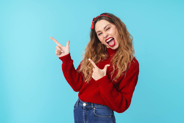 Image of excited caucasian woman in headband laughing and pointing fingers aside isolated over blue background - Photo, image