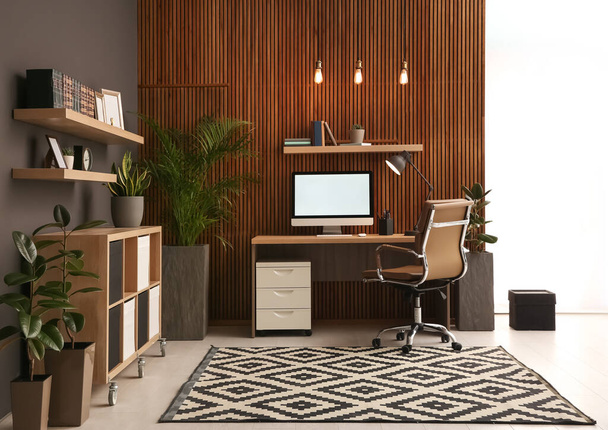 Comfortable workplace with computer near wooden wall in stylish room interior. Home office design - Valokuva, kuva