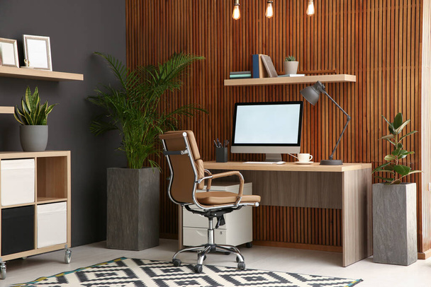 Comfortable workplace with computer near wooden wall in stylish room interior. Home office design - Foto, Bild