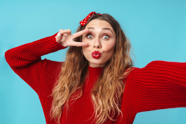 Image of amusing blonde woman gesturing peace sign and taking selfie photo isolated over blue background - Photo, image