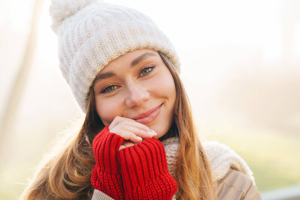 Close up of a cheerful pretty young girl wearing winter jacket and a hat standing on a city street - Fotografie, Obrázek