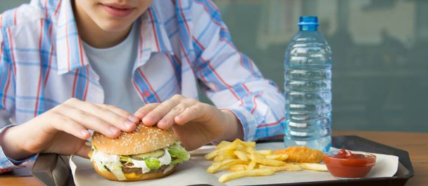 close-up of a girl in a shirt sitting at a table eating fast food, a Burger and fries - Fotoğraf, Görsel