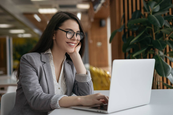 Bizneswoman korzystająca z laptopa, oglądająca szkolenia. Portret szczęśliwego, odnoszącego sukcesy menedżera pracującego w biurze. Piękna kobieta freelancer sobie stylowe okulary siedzi w miejscu pracy  - Zdjęcie, obraz