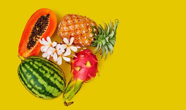 Tropical fruits - pineapple, dragon, watermelon and half papaya on a yellow background. Tropical flower. Space for text - Fotografie, Obrázek