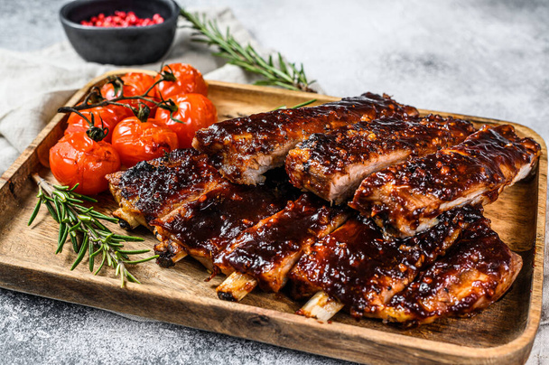 Delicious barbecued ribs seasoned with a spicy basting sauce and served with baked tomatoes. Gray background. Top view. - 写真・画像