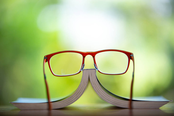 Orange eyeglasses with a book on wooden table, Bokeh garden background, Close up & Macro shot, Selective focus, Stationery concept - Zdjęcie, obraz