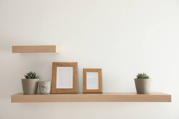 Wooden shelves with plants and photo frames  on light wall - Φωτογραφία, εικόνα