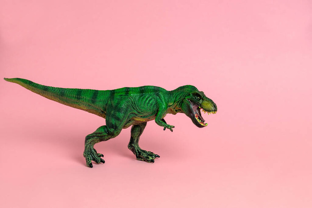 green dinosaur toy with open mouth on a pastel pink  background - Φωτογραφία, εικόνα