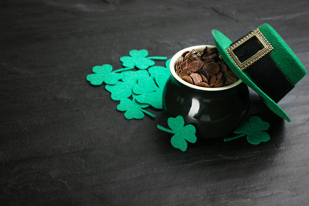 Pot of gold coins, hat and clover leaves on black stone table, space for text. St. Patrick's Day celebration - Foto, immagini