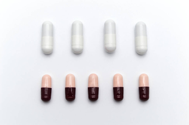 Los medicamentos recetados, cápsulas de diferentes colores entre cápsulas blancas y marrón rojizo oscuro y rosa suave se mezclan. Sobre fondo blanco
. - Foto, Imagen