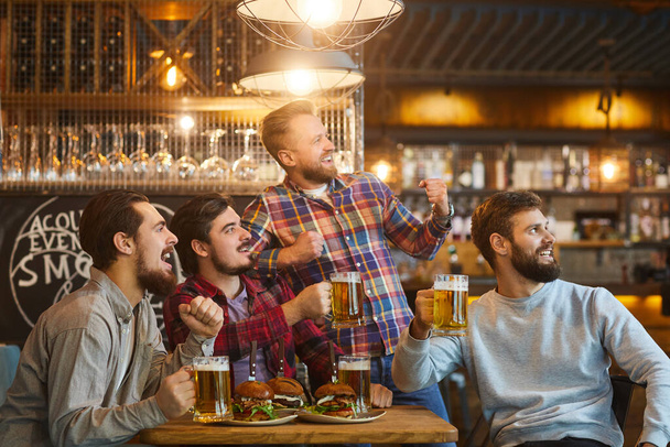 A group of guys watching sports on tv in a pub bar. - Фото, зображення