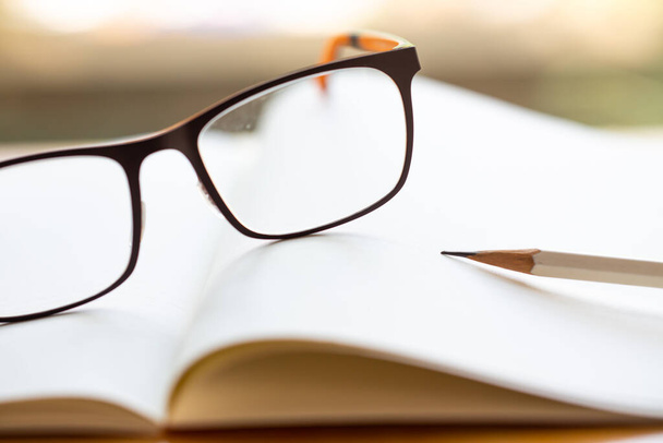Czarne okulary, biały ołówek z białym notebookiem na drewnianym stole, zbliżenie i ujęcie makro, ostrość selektywna, koncepcja piśmiennictwa - Zdjęcie, obraz