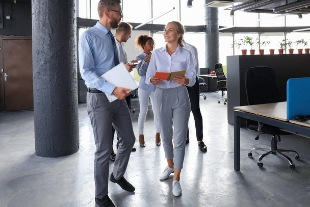 Gruppe moderner Geschäftsleute spricht und lächelt, während sie im Büroflur steht - Foto, Bild