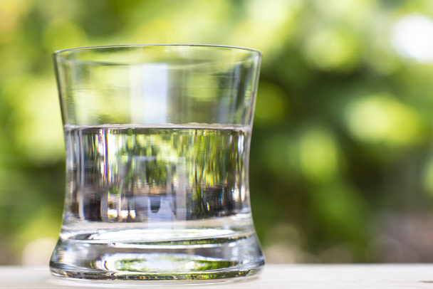 Transparent glass of clean water on wood table in bokeh green garden background, Close up & Macro shot, Selective focus, Healthy Drink concept - Fotoğraf, Görsel